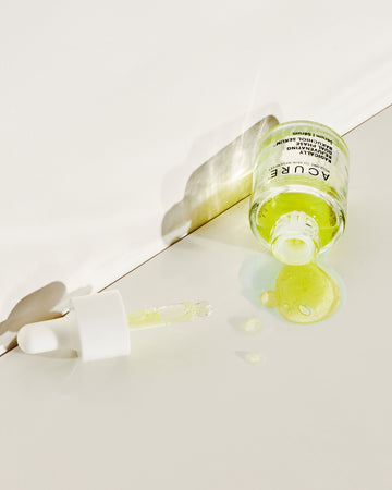 Bottle of Acure Bakuchoil serum laying on a white base with liquid and dropper